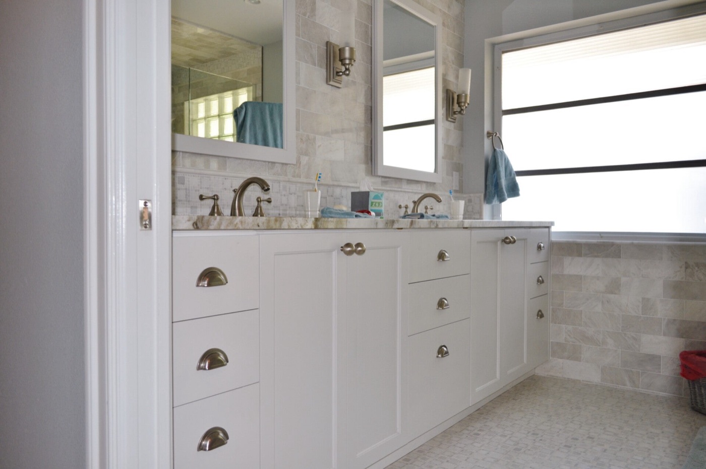 Bathroom with a long white shaker double vanity, marble tile surround, framed mirrors and brushed nickel fixtures.