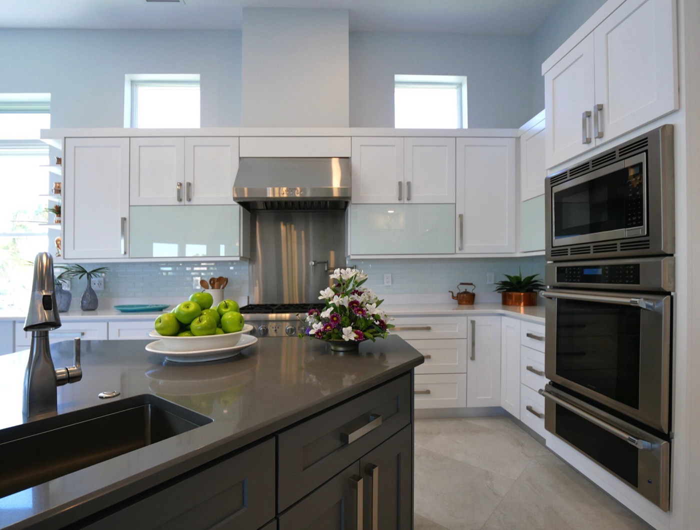 Modern kitchen with white and grey shaker cabinets, frosted glass upper doors, quartz counters and a stainless wall oven.